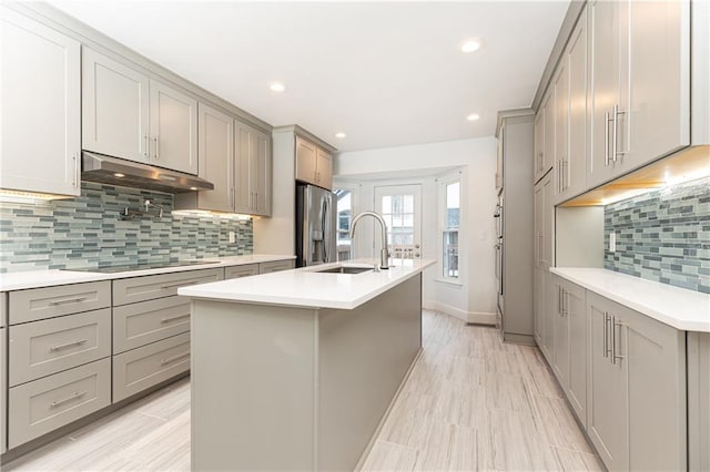 kitchen with a sink, black electric cooktop, under cabinet range hood, and gray cabinetry