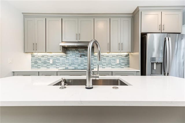 kitchen featuring gray cabinetry, stainless steel fridge, a sink, and tasteful backsplash