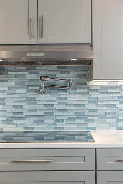 interior details with under cabinet range hood, gray cabinetry, decorative backsplash, and light countertops