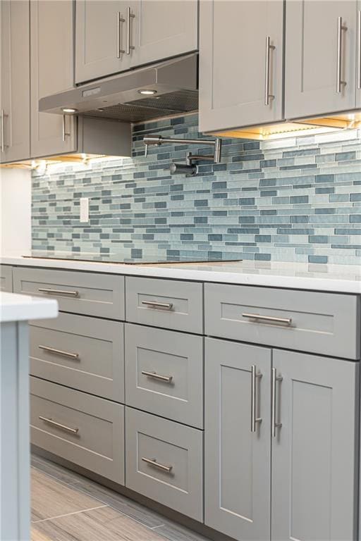 kitchen with under cabinet range hood, gray cabinetry, tasteful backsplash, and light countertops