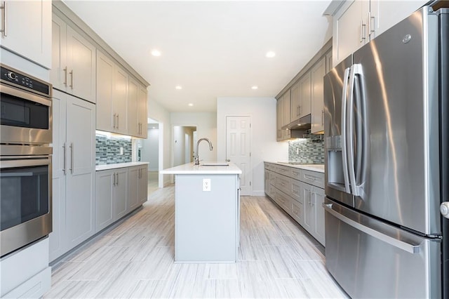 kitchen featuring appliances with stainless steel finishes, a sink, decorative backsplash, under cabinet range hood, and gray cabinetry