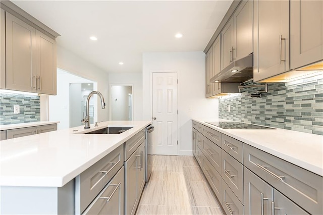 kitchen featuring under cabinet range hood, stainless steel dishwasher, gray cabinetry, and a sink