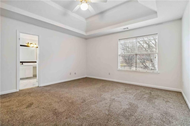 unfurnished bedroom featuring ceiling fan, ensuite bath, a tray ceiling, and carpet floors