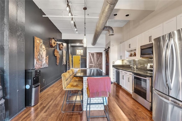 kitchen featuring appliances with stainless steel finishes, a barn door, rail lighting, and white cabinetry