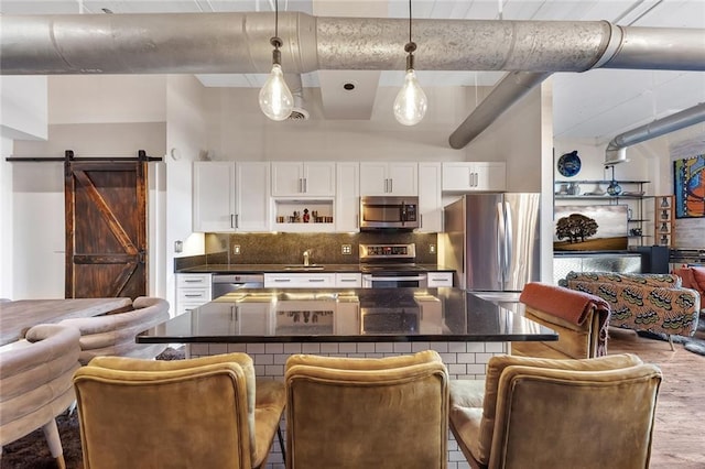 kitchen with a kitchen breakfast bar, a barn door, appliances with stainless steel finishes, decorative light fixtures, and white cabinetry