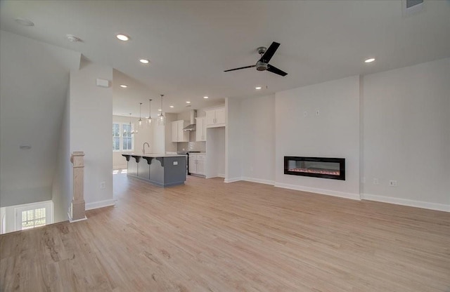 unfurnished living room featuring ceiling fan, sink, and light hardwood / wood-style flooring