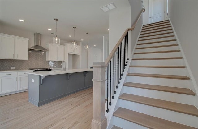 kitchen featuring wall chimney range hood, a breakfast bar, a kitchen island with sink, hanging light fixtures, and white cabinets