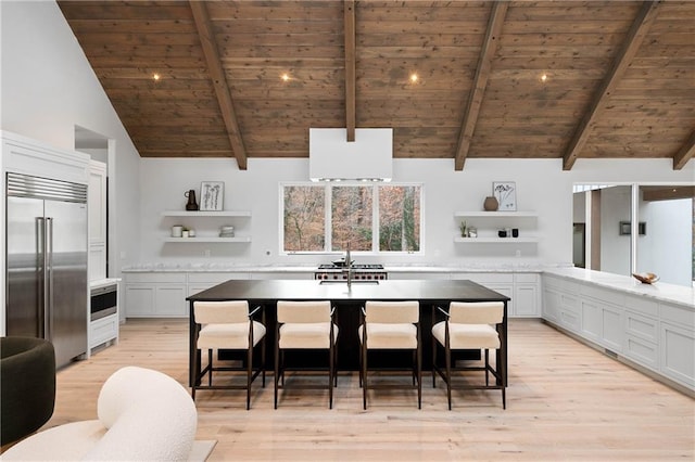 kitchen with white cabinetry, wooden ceiling, beamed ceiling, stainless steel built in refrigerator, and a breakfast bar