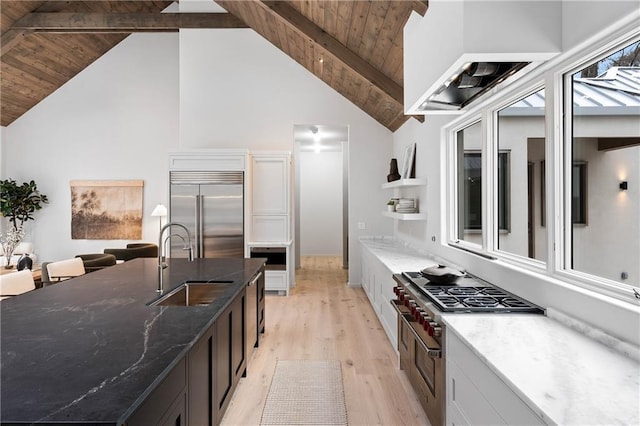 kitchen with vaulted ceiling with beams, built in refrigerator, sink, and dark stone counters