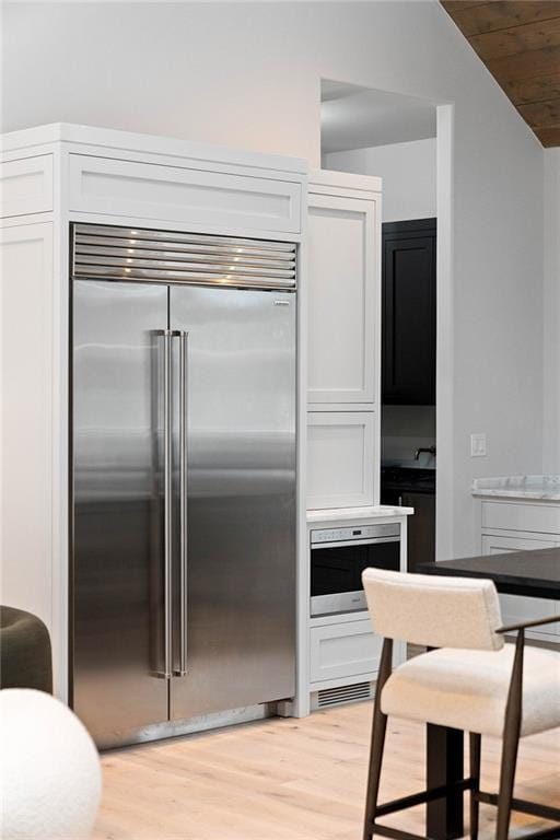 kitchen featuring built in refrigerator, white cabinets, wooden ceiling, and lofted ceiling