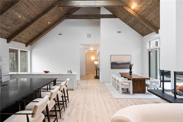 dining space featuring beam ceiling, light hardwood / wood-style floors, high vaulted ceiling, and wooden ceiling