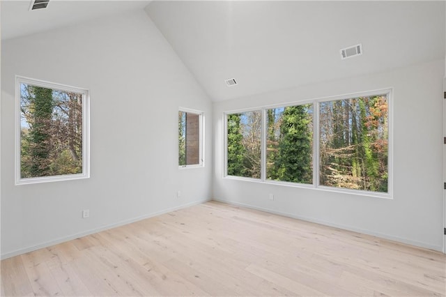 empty room featuring plenty of natural light, lofted ceiling, and light wood-type flooring