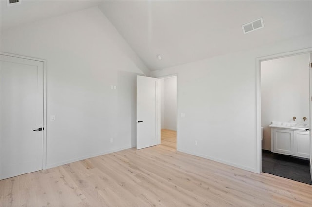 unfurnished bedroom with ensuite bathroom, light wood-type flooring, and high vaulted ceiling