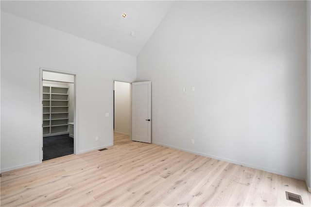 unfurnished bedroom with light wood-type flooring, a walk in closet, high vaulted ceiling, and a closet