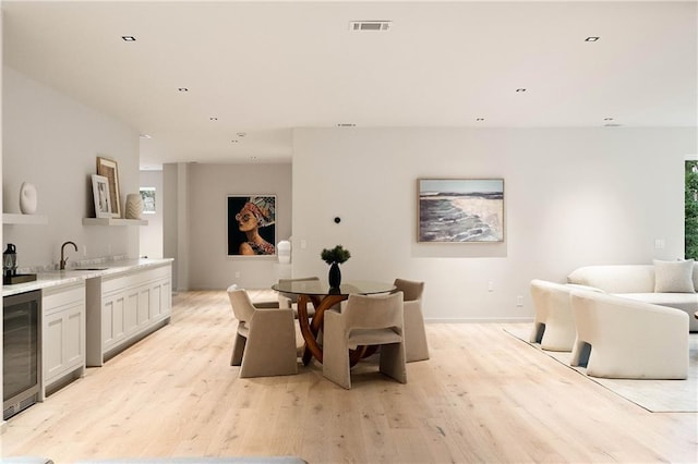 dining space with light wood-type flooring, sink, and wine cooler