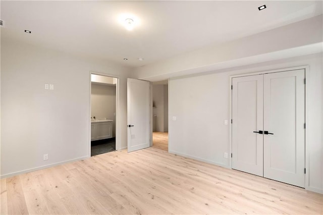 unfurnished bedroom featuring a closet, ensuite bathroom, and light hardwood / wood-style flooring