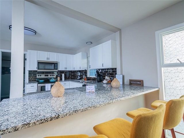 kitchen with appliances with stainless steel finishes, white cabinetry, a peninsula, and a breakfast bar area