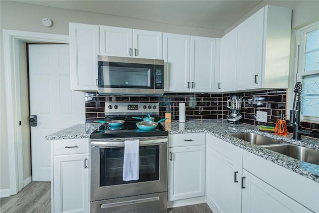 kitchen with appliances with stainless steel finishes, a sink, light wood-type flooring, white cabinetry, and backsplash