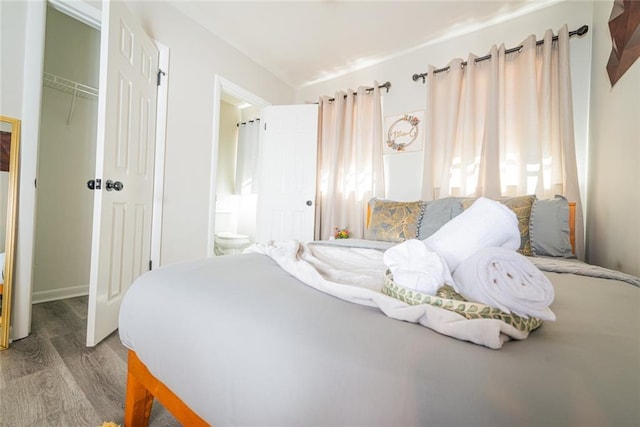 bedroom featuring ensuite bath, a closet, wood finished floors, and multiple windows