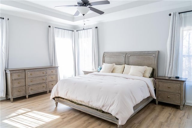 bedroom featuring crown molding, light wood-type flooring, a raised ceiling, and ceiling fan