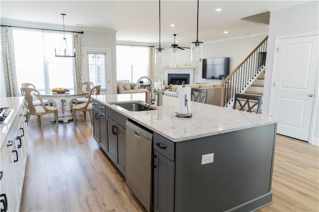 kitchen with ornamental molding, a sink, stainless steel dishwasher, light wood-style floors, and a fireplace