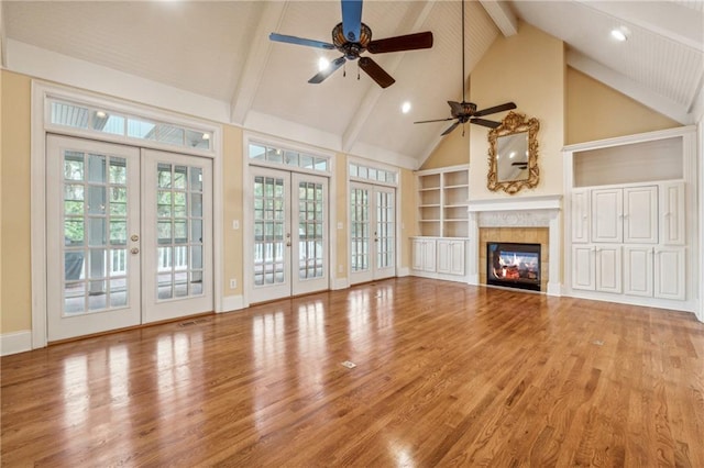 unfurnished living room featuring ceiling fan, beam ceiling, wood-type flooring, and french doors