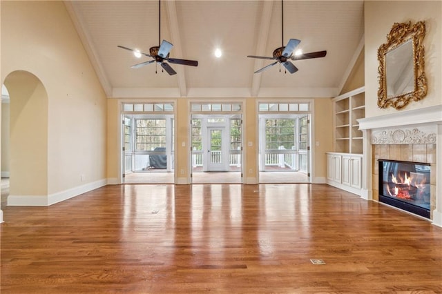 unfurnished living room featuring wood-type flooring, a healthy amount of sunlight, and a tiled fireplace