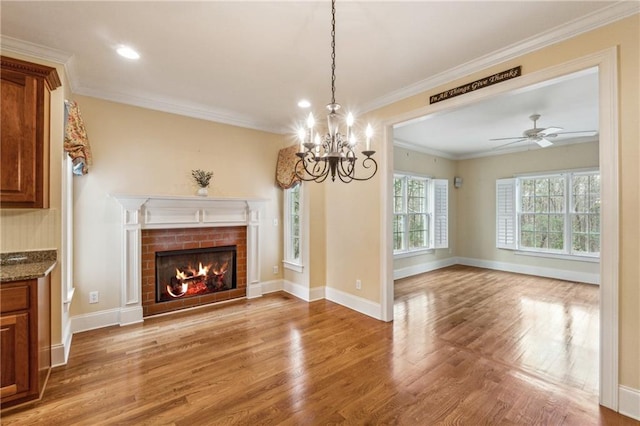 unfurnished living room with crown molding, a fireplace, wood-type flooring, and ceiling fan with notable chandelier