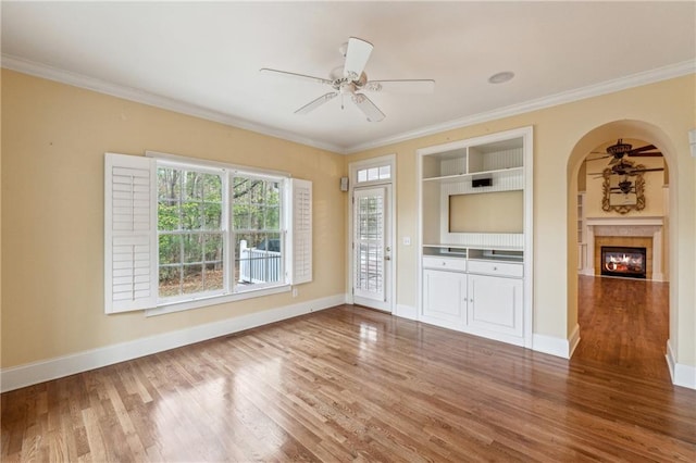 unfurnished living room with hardwood / wood-style floors, ceiling fan, built in features, and crown molding