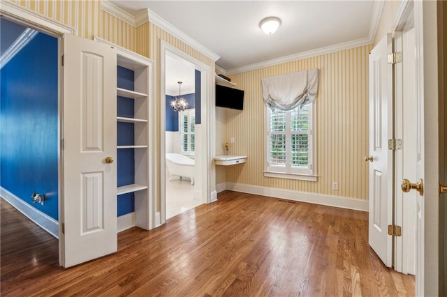 unfurnished bedroom featuring hardwood / wood-style flooring, ensuite bath, crown molding, and a chandelier