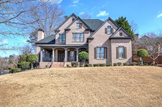 french country style house with a porch, a chimney, a front lawn, and brick siding