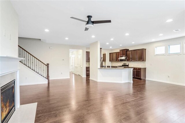 kitchen featuring gas stove, stone countertops, dark brown cabinets, dark hardwood / wood-style flooring, and decorative backsplash