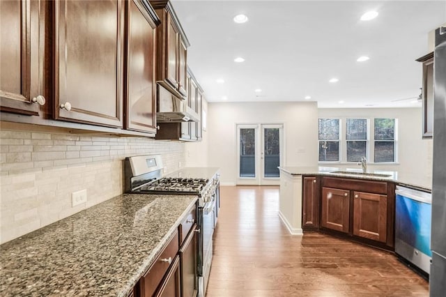 kitchen featuring sink, dark wood-type flooring, appliances with stainless steel finishes, light stone countertops, and decorative backsplash