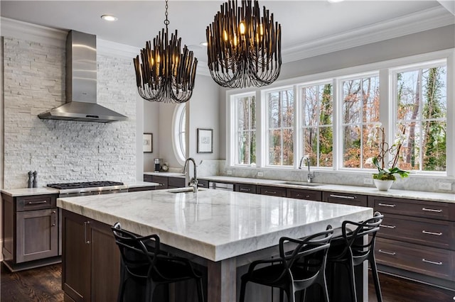 kitchen with sink, a kitchen island with sink, wall chimney range hood, and a kitchen bar