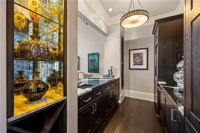 bar with sink, crown molding, dark wood-type flooring, dark brown cabinetry, and dark stone counters