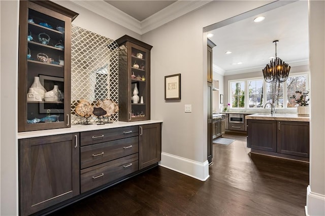 bar featuring pendant lighting, ornamental molding, a notable chandelier, dark brown cabinetry, and dark wood-type flooring