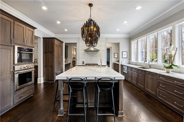 kitchen featuring sink, hanging light fixtures, dark hardwood / wood-style floors, light stone counters, and a center island with sink