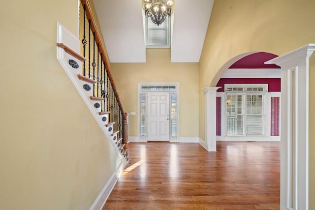 entrance foyer with a chandelier, wood-type flooring, a towering ceiling, and decorative columns