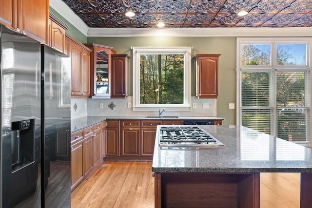 kitchen featuring light wood-type flooring, ornamental molding, black fridge with ice dispenser, stainless steel gas cooktop, and sink