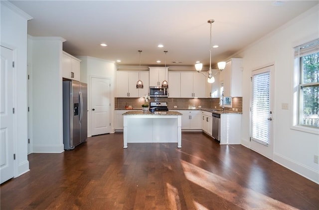 kitchen featuring appliances with stainless steel finishes, a kitchen island, white cabinets, decorative light fixtures, and backsplash