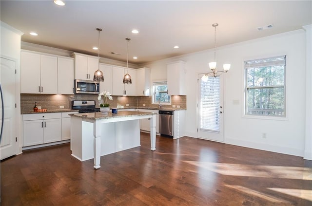 kitchen with appliances with stainless steel finishes, pendant lighting, white cabinetry, and a kitchen island