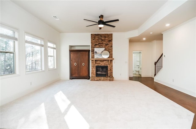 living room featuring hardwood / wood-style flooring, ceiling fan, ornamental molding, and a stone fireplace