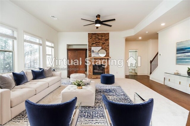 living room with ceiling fan, a stone fireplace, crown molding, and hardwood / wood-style flooring