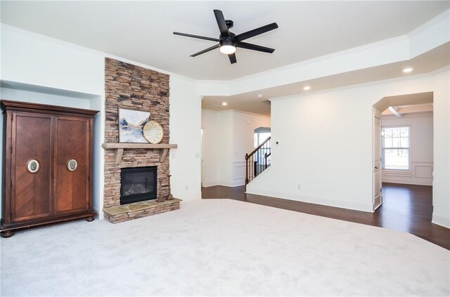 unfurnished living room featuring ceiling fan, dark wood-type flooring, a stone fireplace, and crown molding