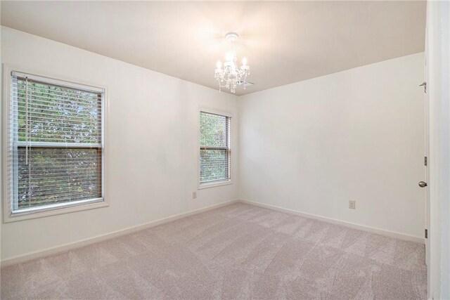 unfurnished room featuring light colored carpet, a notable chandelier, and a healthy amount of sunlight