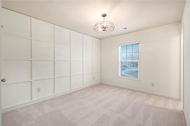 spare room featuring an inviting chandelier and light colored carpet