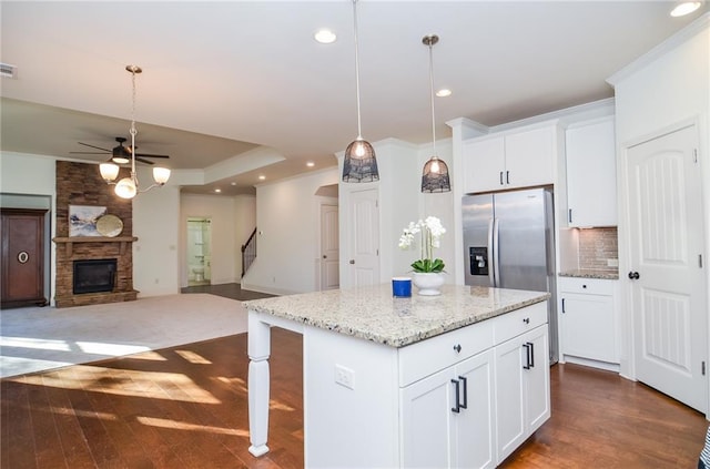 kitchen with hanging light fixtures, stainless steel fridge, white cabinetry, ceiling fan, and a stone fireplace