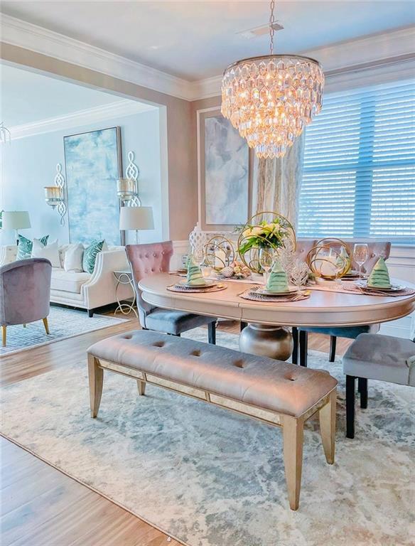 dining space featuring wood-type flooring, ornamental molding, and an inviting chandelier