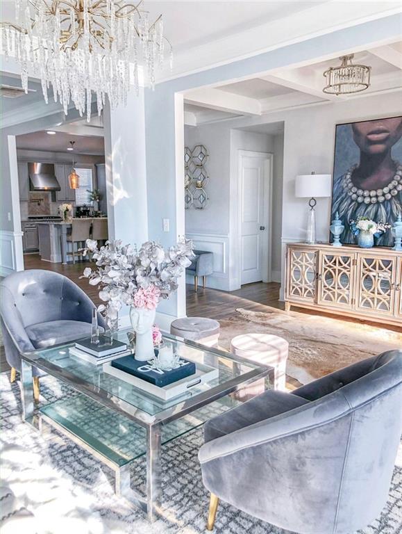 living room with beamed ceiling, hardwood / wood-style floors, ornamental molding, and a notable chandelier