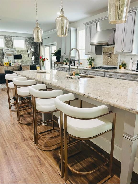 kitchen with tasteful backsplash, gray cabinetry, wall chimney range hood, light hardwood / wood-style flooring, and hanging light fixtures